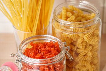 Variety of dry italian pasta in glass jars on kitchen cabinet with wooden top: fusilli, tagliatelle, farfalle, spaghetti