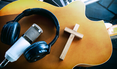 wooden cross with microphone and headphones on acoustic guitar, recording sound of worship online,...
