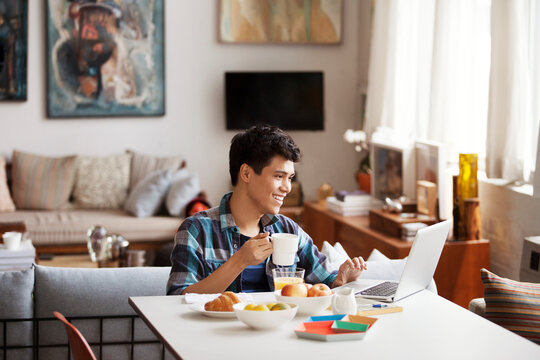 Happy young man using laptop while having coffee at home