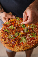 Male hands with tattoos holding a vegetarian clean pizza and adding parsley on top