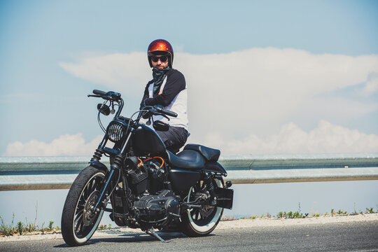 Biker standing by cruiser motorcycle on roadside against sky