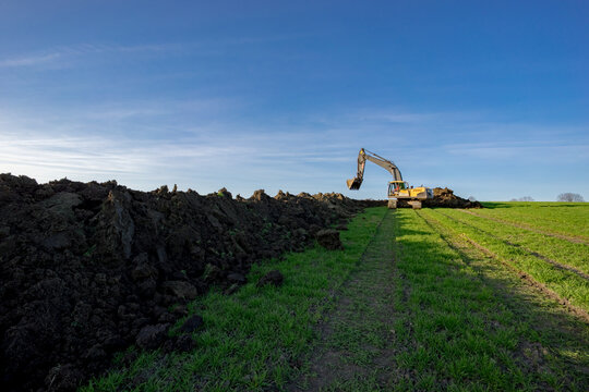 Gelber Bagger hebt das Erdreich aus, vor blauem Himmel.