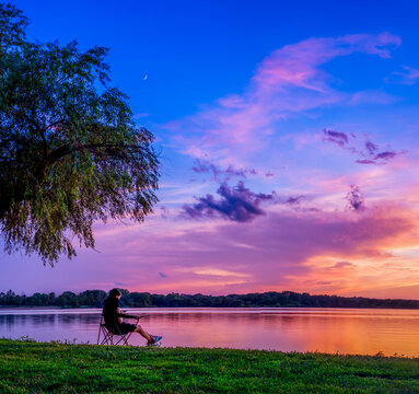Woman using mobile phone while relaxing at lakeshore against dramatic sky