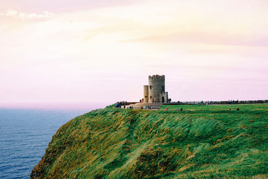 Tourist visiting Obrien Tower on Cliffs Of Moher by sea against cloudy sky