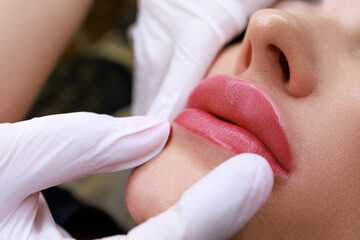 close-up of a permanent make-up master holding the lips of a model showing the completed work of permanent make-up of the lips - obrazy, fototapety, plakaty