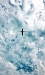 The plane is flying in the cloudy sky. The sun shines. 