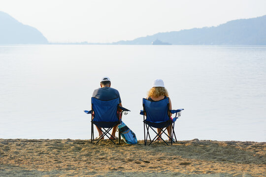 A man and a woman sit on chairs near the sea and look at the sea bay. Family quarrel. Spat between a married couple.