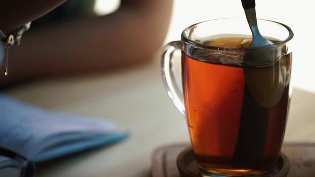 Close-up view of the girl hand stirring the tea with lemon and cinnamon while sitting in the cafe.