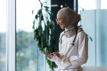 Female doctor in hijab works in modern clinic office, Muslim female doctor uses tablet computer,...