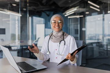 Portrait of successful muslim female doctor in hijab, arabic woman working in modern clinic office, smiling and looking at camera, female doctor in glasses and white medical coat with stethoscope.