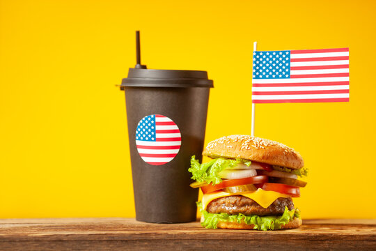 Close-up home made beef burger with american flag on the top and cup on wooden table over orange background