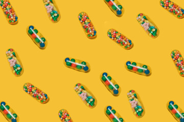 Vibrant colorful pattern of medicine pill capsules filled with sugar candy sprinkles on yellow background. Creative concept of overdose medicine usage and addiction to food supplement. Placebo.