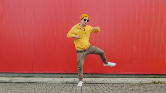 Playful crazy man dance emotions. Dancing man funny break dance, happy rhythmically waving his arms against red textured street wall. Breakdancing, street dancing, hiphop, freestyle dance. Lifestyle 