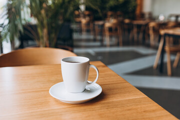 A Cup of freshly brewed black tea at a cafe blurred background. Coffee cup on table cafe shop Interior. Concept of easy breakfast. One white big ceramic cup.
