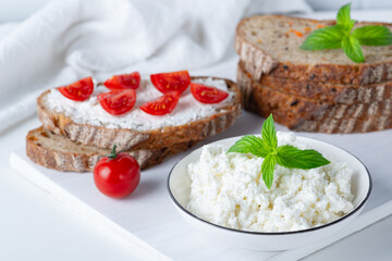 Fototapeta na wymiar Slices of bread with cottage cheese and cherry tomatoes on wooden cutting board on white background