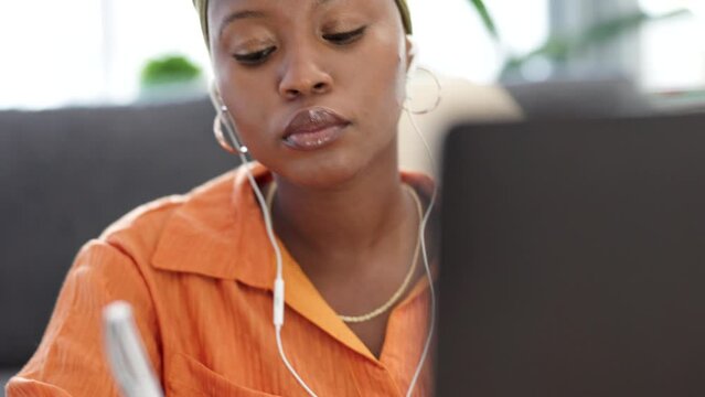Music streaming, writing and computer research of a woman from Nigeria multitask on a home sofa. Working, planning and notebook summary of a female studying and learning a phd report in a living room