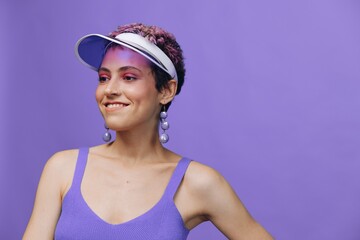 Portrait of a sporty fashion woman posing smiling in a purple sports suit for yoga and a transparent cap on a purple background monochrome
