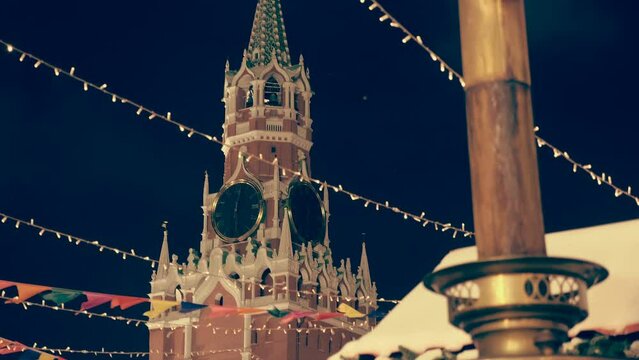 Festive garlands and a large metal samovar with a smoke chimney against the Kremlin Spasskaya Tower with a clock at the fair on Red Square create a festive, New Year's mood