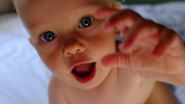 Cute baby with blond hair smiling, stretching a hand to the camera. 1 year old child portrait. Slow motion video