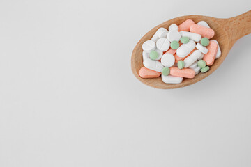 Many different pills in wooden spoon on white background. Copy space. Top view