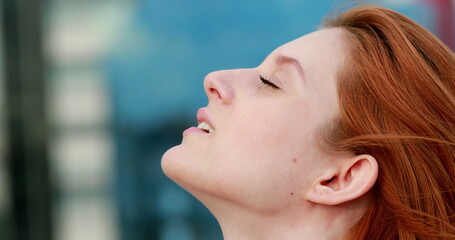 Young redhair woman looking up in the sky, opening and closing eyes