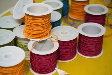 Stapel Spulen mit orangenem und rotem Gummigarn auf gelbem Tisch 