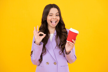 Funny face. Teenager girl holding a hot cup of coffee or tea. Child with takeaway cup on yellow...