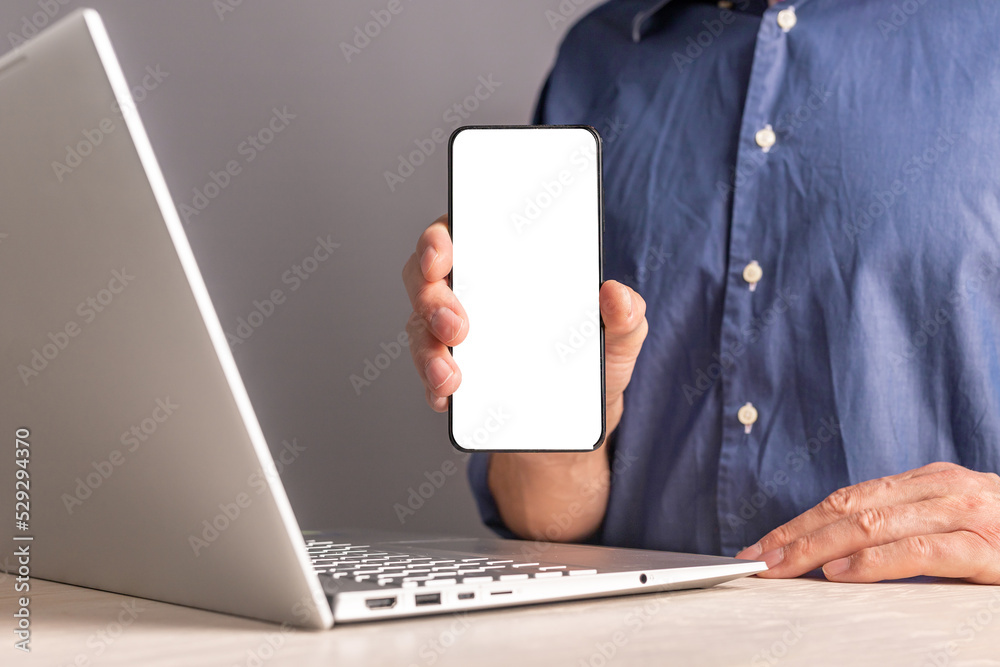 Poster Man showing phone mockup. Male sitting at table with laptop and presenting mobile app at smartphone with white screen. Application advertisement