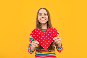 Cheerful lovely romantic teen girl hold red heart symbol of love for valentines day isolated on yellow background.