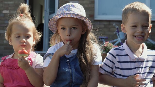 Three cute little Children enjoys delicious ice cream cone. Child eating watermelon popsicle. Kids Siblings snack sweets in Home Garden. Summer holiday Hot weather Sunny Day. Childhood, Food Candy