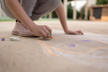 Girl draws with colorful crayons on pavement. Children's drawings with chalk on wall. Creative kid. Joy of childhood. High quality photo