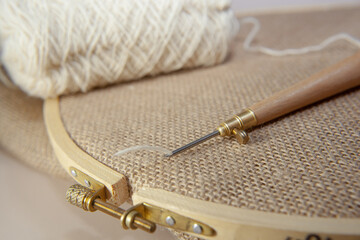 Punch needle with a burlap fabric in a embroidery hoop and a threaded needle with a woolen thread