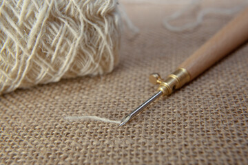 Punch needle with a burlap fabric in a embroidery hoop and a threaded needle with a woolen thread