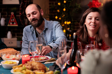 Couple celebrating christmas with family, talking at festive dinner table, eating traditional winter holiday meal, drinking sparkling wine. Xmas celebration at home party, wife and husband chatting