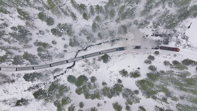 4K Aerial overhead view steam locomotive goes over winter snowy woodland. Follow shot, moving left. Snowy winter day Colorado canyon. Top down aerial shot of railway train in snow covered forest trees