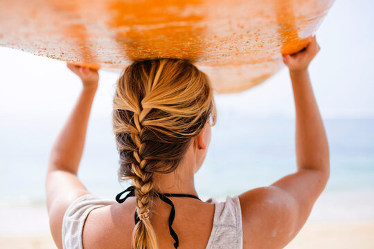 Rear view of woman carrying surfboard on head at beach
