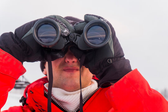 Close-up of man looking through binoculars while standing on snow covered field