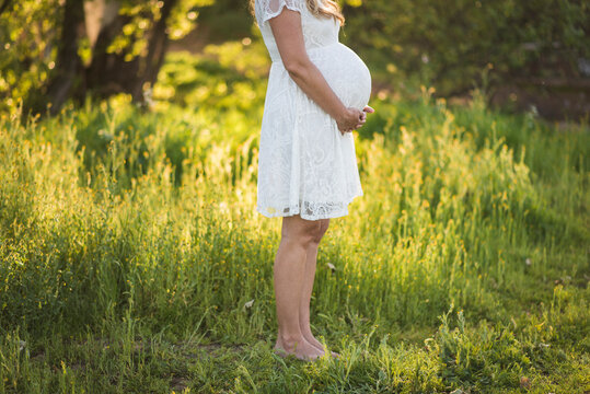 Low section of pregnant woman touching abdomen while standing on grassy field in park
