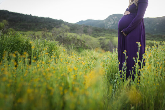 Midsection of pregnant woman touching abdomen while standing on grassy field in park