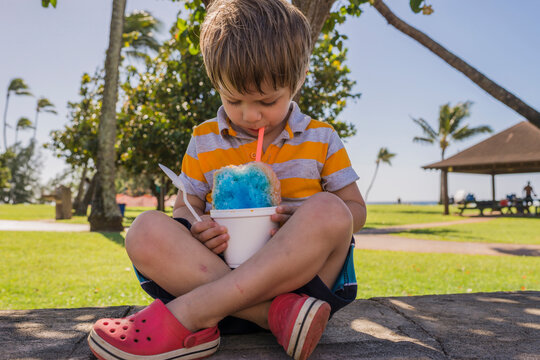 Boy eating slush while sitting on footpath at park