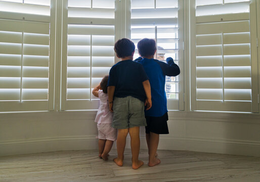 Siblings looking through window blinds at home