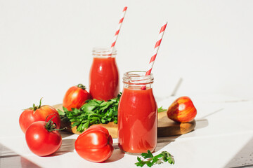Tomato juice in bottles and fresh red tomatoes on a white wooden table. Healthy vegan food. Close-up, selective focus
