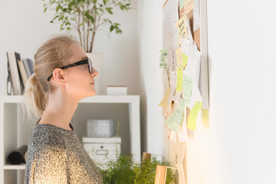 Side view of businesswoman reading adhesive notes on bulletin board in creative office