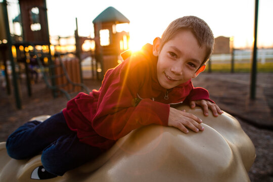 Portrait Of Happy Boy Playing On Animal Statue At Playground During Sunset