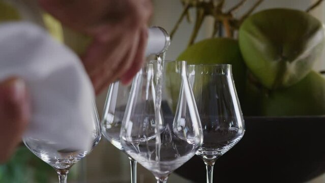 Host's hands pouring white wine in glasses on table of tropical beach resort