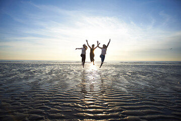 Female friends jumping at beach against sky