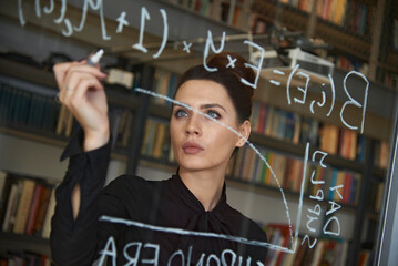 Businesswoman writing formula on glass wall