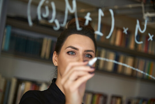 Businesswoman writing formula on glass wall at office