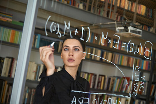 Serious businesswoman writing formula on glass wall at office