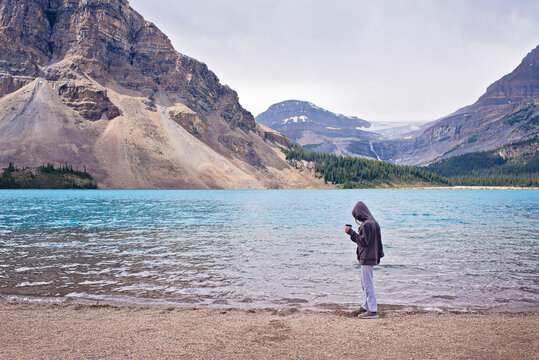 Side view of woman wearing hooded shirt holding cup while standing at lakeshore against sky - Powered by Adobe